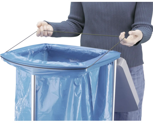 Person befestigt einen blauen Müllbeutel mit einer Schnur an einem Abfallsammler aus Metall.