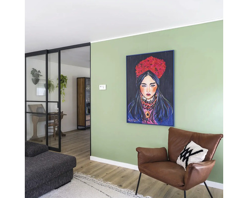 Wohnzimmer mit grüner Wand, gerahmtem Gemälde einer Frau, braunem Ledersessel und schwarzer Glastür zum angrenzenden Raum.