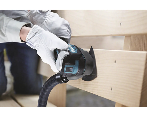 Eine Person mit weißen Arbeitshandschuhen schneidet mit einem Makita Multifunktionswerkzeug mit Sägeblatt und Staubabsaugung eine Holzplanke.