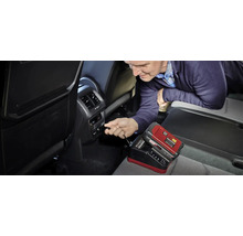 Ein Mann schließt ein Einhell Power X-Change Ladegerät für 18 Volt Akkus an den 12 Volt Anschluss im Innenraum eines Autos an.