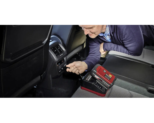 Ein Mann schließt ein Einhell Power X-Change Ladegerät für 18 Volt Akkus an den 12 Volt Anschluss im Innenraum eines Autos an.