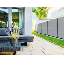 Moderner Sichtschutzzaun aus hellgrauen Paneelen mit dunklen Pfosten in einem Garten neben einer Terrasse mit Loungemöbeln und Rasen.