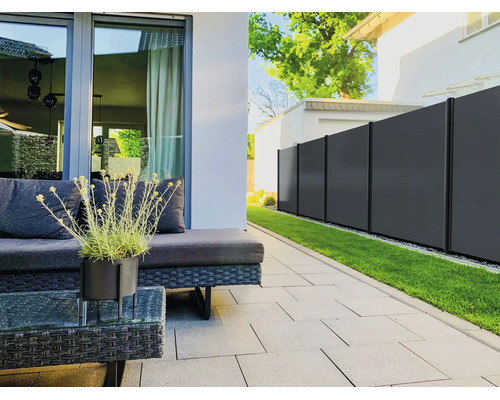 Moderner Sichtschutzzaun in Anthrazit auf einer organisierten Terrasse mit grauen Bodenplatten, Gartenmöbeln aus Geflecht und einer Rasenfläche.