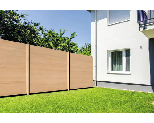 Moderner Sichtschutzzaun aus Wood-Plastic-Composite in Holzoptik, im Garten auf einem Rasen neben einer weißen Hauswand installiert.