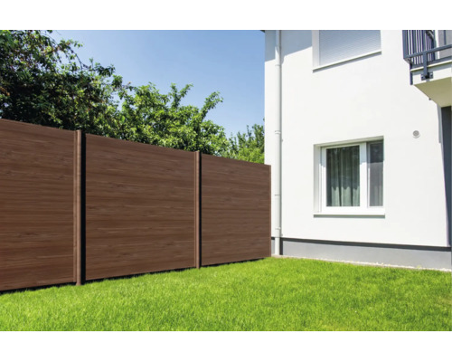 Moderner Sichtschutzzaun in Holzoptik aus Verbundwerkstoff im Garten neben einer weißen Hauswand.