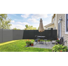 Moderner Sichtschutzzaun in Anthrazit auf einer hellen Terrasse mit Gartenmöbeln, Blumenkübeln und angrenzendem Rasen.
