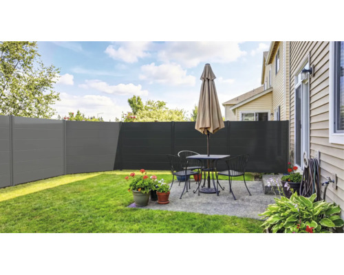 Moderner Sichtschutzzaun in Anthrazit auf einer hellen Terrasse mit Gartenmöbeln, Blumenkübeln und angrenzendem Rasen.