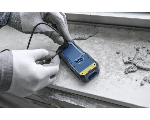 Eine Person mit Arbeitshandschuhen schließt ein USB-Kabel an ein Feuchtigkeitsmessgerät an.