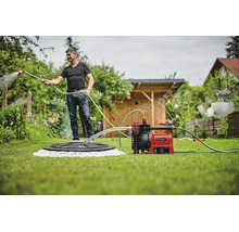 Ein Mann bewässert den Garten mit einer automatischen Gartenpumpe von Einhell, die an eine Zisterne angeschlossen ist.
