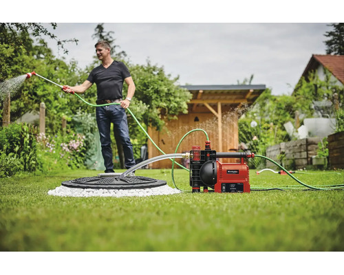 Ein Mann bewässert den Garten mit einer automatischen Gartenpumpe von Einhell, die an eine Zisterne angeschlossen ist.