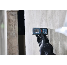 Eine Person mit Arbeitshandschuhen verwendet einen digitalen Laser Entfernungsmesser von Bosch an einer Betonwand.