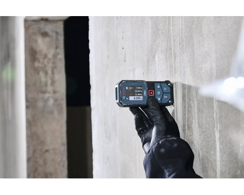Eine Person mit Arbeitshandschuhen verwendet einen digitalen Laser Entfernungsmesser von Bosch an einer Betonwand.