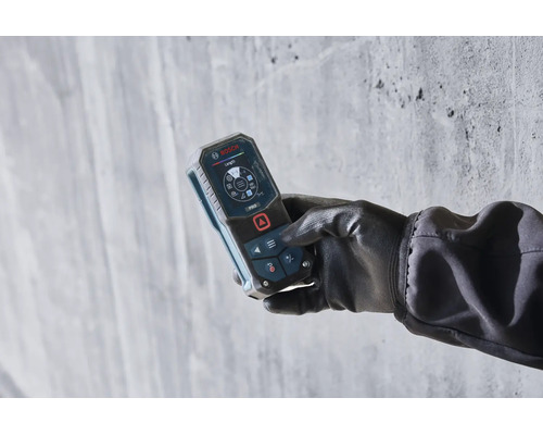 Eine Hand mit Handschuh hält ein Bosch Laser-Entfernungsmessgerät mit digitalem Display vor einer Betonwand.
