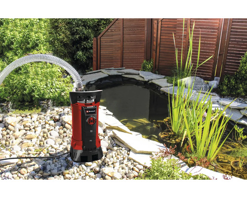 Einhell Schmutzwasserpumpe mit Schlauch an einem Gartenteich mit Steinen und Pflanzen.