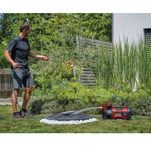 Ein Mann bewässert den Garten mit einer Akku-Gartenpumpe von Einhell, die Wasser aus einer Zisterne pumpt.