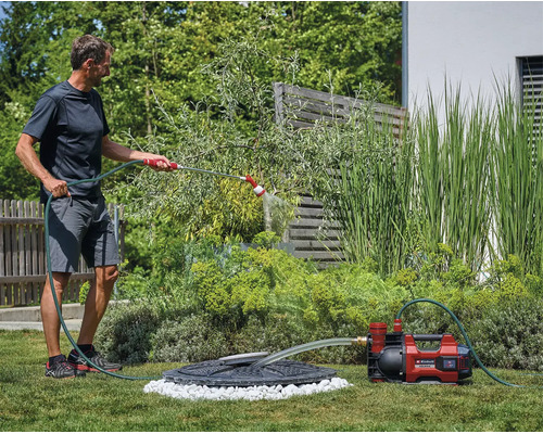 Ein Mann bewässert den Garten mit einer Akku-Gartenpumpe von Einhell, die Wasser aus einer Zisterne pumpt.