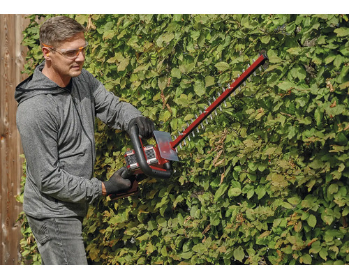 Ein Mann schneidet eine Hecke mit einer Akku-Heckenschere und trägt dabei Sicherheitsausrüstung.
