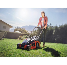 Frau mäht den Rasen in einem sonnigen Garten mit einem Einhell Akku-Rasenmäher.