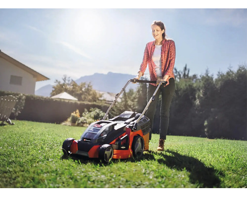 Frau mäht den Rasen in einem sonnigen Garten mit einem Einhell Akku-Rasenmäher.