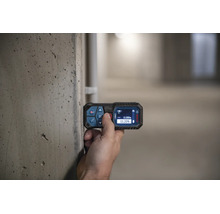 Eine Hand bedient einen Bosch Laser Entfernungsmesser an einer Betonwand mit Messanzeige auf dem Display.