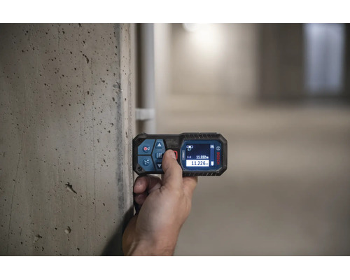 Eine Hand bedient einen Bosch Laser Entfernungsmesser an einer Betonwand mit Messanzeige auf dem Display.
