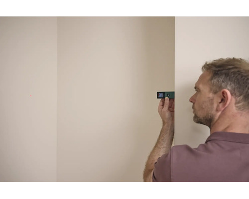 Ein Mann verwendet einen digitalen Laserentfernungsmesser von Bosch gegen eine Wand, um eine Distanz zu messen.