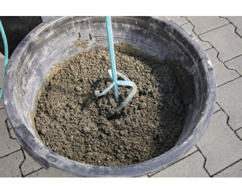 Beton mischen im Mörtelkübel mit einem Rührwerk auf Pflastersteinen.