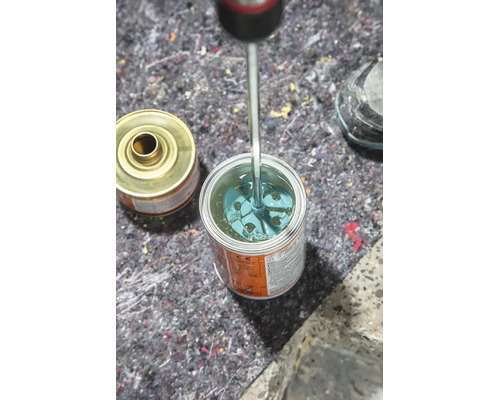 Ein Schraubendreher wird in eine geöffnete Metalldose mit Flüssigkeit eingeführt, um den Inhalt umzurühren.