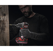 Handwerker mit Schutzbrille benutzt einen Akku-Bohrschrauber von Einhell, um eine Schraube in einen Holzpfahl zu drehen.