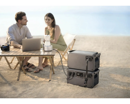 Tragbare Powerstations im Einsatz am Strand, versorgen Laptop und Kaffeemaschine auf einem Campingtisch mit Strom.