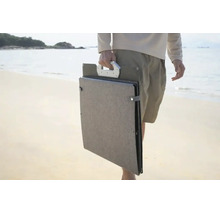 Tragbares, zusammengefaltetes Solarpanel mit Tragegriff, getragen von einer Person am Strand.