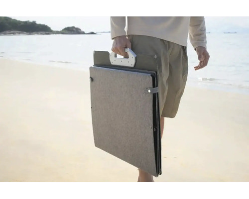 Tragbares, zusammengefaltetes Solarpanel mit Tragegriff, getragen von einer Person am Strand.