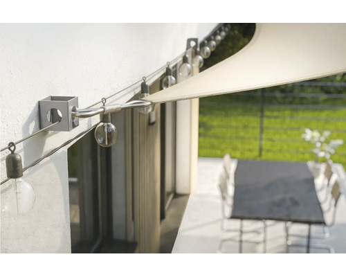 Wandhalterung für Sonnensegel mit gespanntem Drahtseil und einer Lichterkette über einer Terrasse.