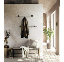 Moderne Wandgarderobe mit zwei Edelstahlstangen im hellen Flur mit Holzelementen, einer Sitzbank und einer Zimmerpflanze.