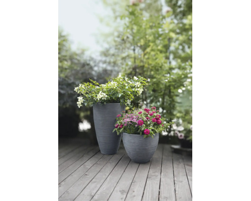 Zwei graue, gerillte Pflanzkübel mit blühenden Blumen auf einer Holzterrasse im Garten.