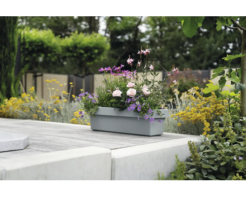 Bepflanzter grauer Blumenkasten auf einer gepflasterten Terrasse im Garten.
