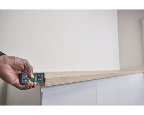 Eine Person misst mit einem Bosch Laser Entfernungsmesser die Länge einer Regalkante an einem modernen Möbelstück.