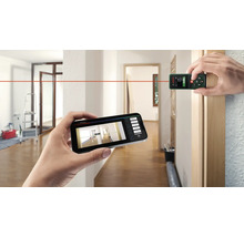Ein digitaler Bosch Laser Entfernungsmesser wird in einem Innenraum zur Messung genutzt und überträgt die Daten per App auf ein Smartphone.
