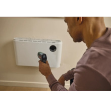 Eine Person misst die Temperatur eines Wandheizgerätes mit einem Bosch Infrarot Thermometer in einem Innenraum.
