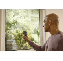 Ein Mann misst die Temperatur an einem Fensterrahmen mit einem Bosch Thermodetektor.