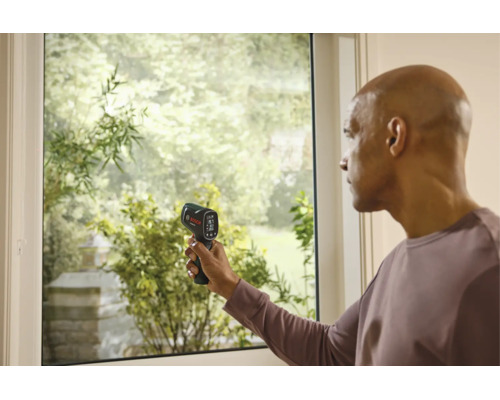 Ein Mann misst die Temperatur an einem Fensterrahmen mit einem Bosch Thermodetektor.