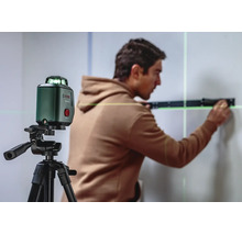 Ein Handwerker nutzt einen grünen Bosch Kreuzlinienlaser auf einem Stativ für präzise Ausrichtungsarbeiten an einer Wand.