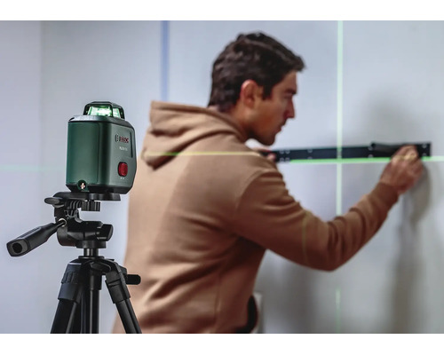 Ein Handwerker nutzt einen grünen Bosch Kreuzlinienlaser auf einem Stativ für präzise Ausrichtungsarbeiten an einer Wand.