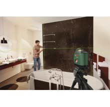 Ein Handwerker nutzt einen Bosch Kreuzlinienlaser auf einem Stativ, um eine Badezimmerwand mit dunklen Marmorfliesen präzise auszurichten.