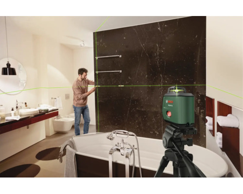Ein Handwerker nutzt einen Bosch Kreuzlinienlaser auf einem Stativ, um eine Badezimmerwand mit dunklen Marmorfliesen präzise auszurichten.