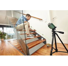 Mann markiert mit einem Bosch Linienlaser auf einem Stativ die Position für eine Wandbeleuchtung an einer Treppe.