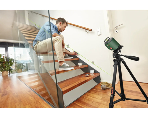 Mann markiert mit einem Bosch Linienlaser auf einem Stativ die Position für eine Wandbeleuchtung an einer Treppe.