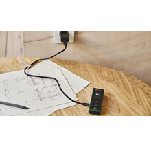 Bosch Laser Entfernungsmesser Zamo wird mit einem USB Kabel an einer Steckdose auf einem Holztisch mit einem Grundrissplan geladen
