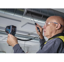 Ein Handwerker prüft mit einem Bosch Thermodetektor die Temperatur an einem Lüftungsschacht in einem Raum.