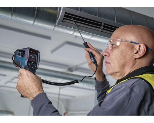 Ein Handwerker prüft mit einem Bosch Thermodetektor die Temperatur an einem Lüftungsschacht in einem Raum.